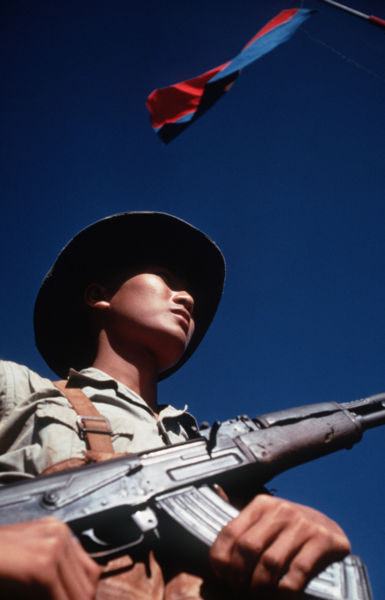 Binh sĩ Việt Cộng (MTGPMN) đứng dưới lá cờ MTGPMN mang khẩu AK-47 tại cuộc trao đổi tù binh của uỷ ban quân sự 4 bên (12/2/1973). Nguồn: SSgt. Herman Kokojan