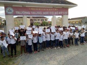 Các em học sinh đứng trước trường đưa biểu ngữ biểu tình (ảnh; facebook Nguyễn Huy Tuấn)